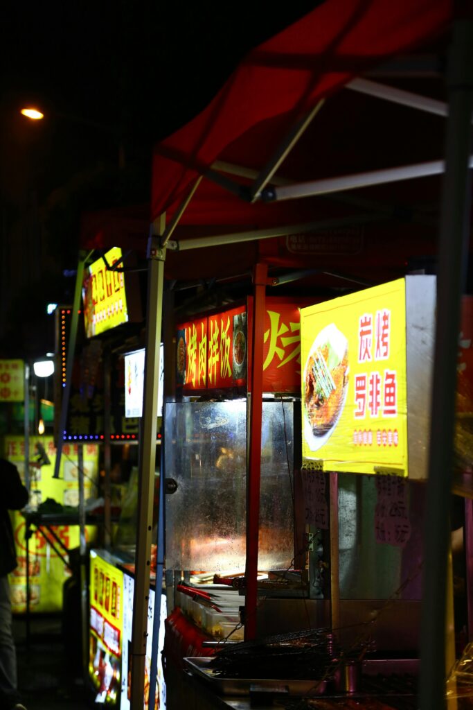 Colorful street food stalls at a lively night market with illuminated signs.