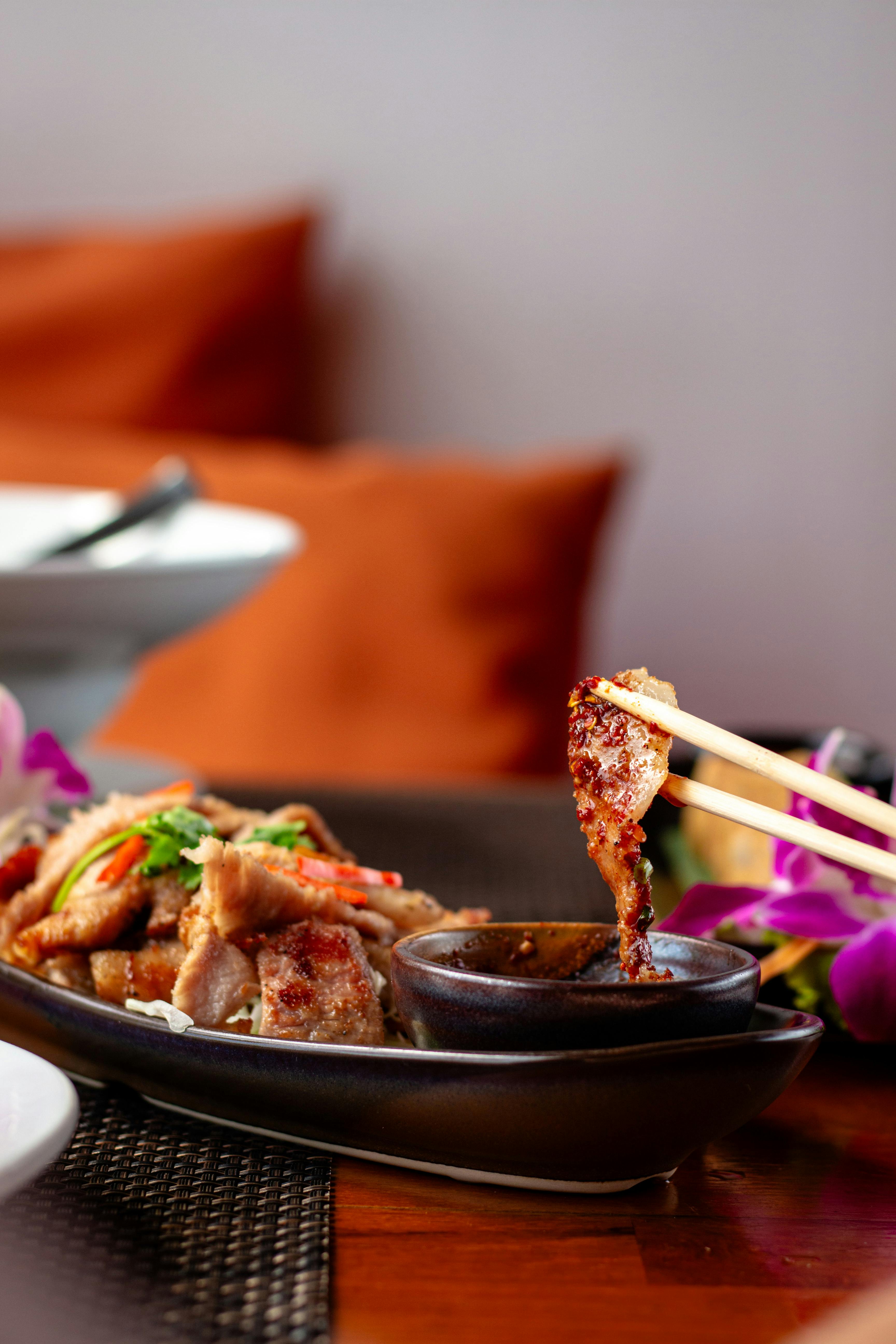 Close-up of a fried dish being dipped into sauce with chopsticks, garnished with herbs.