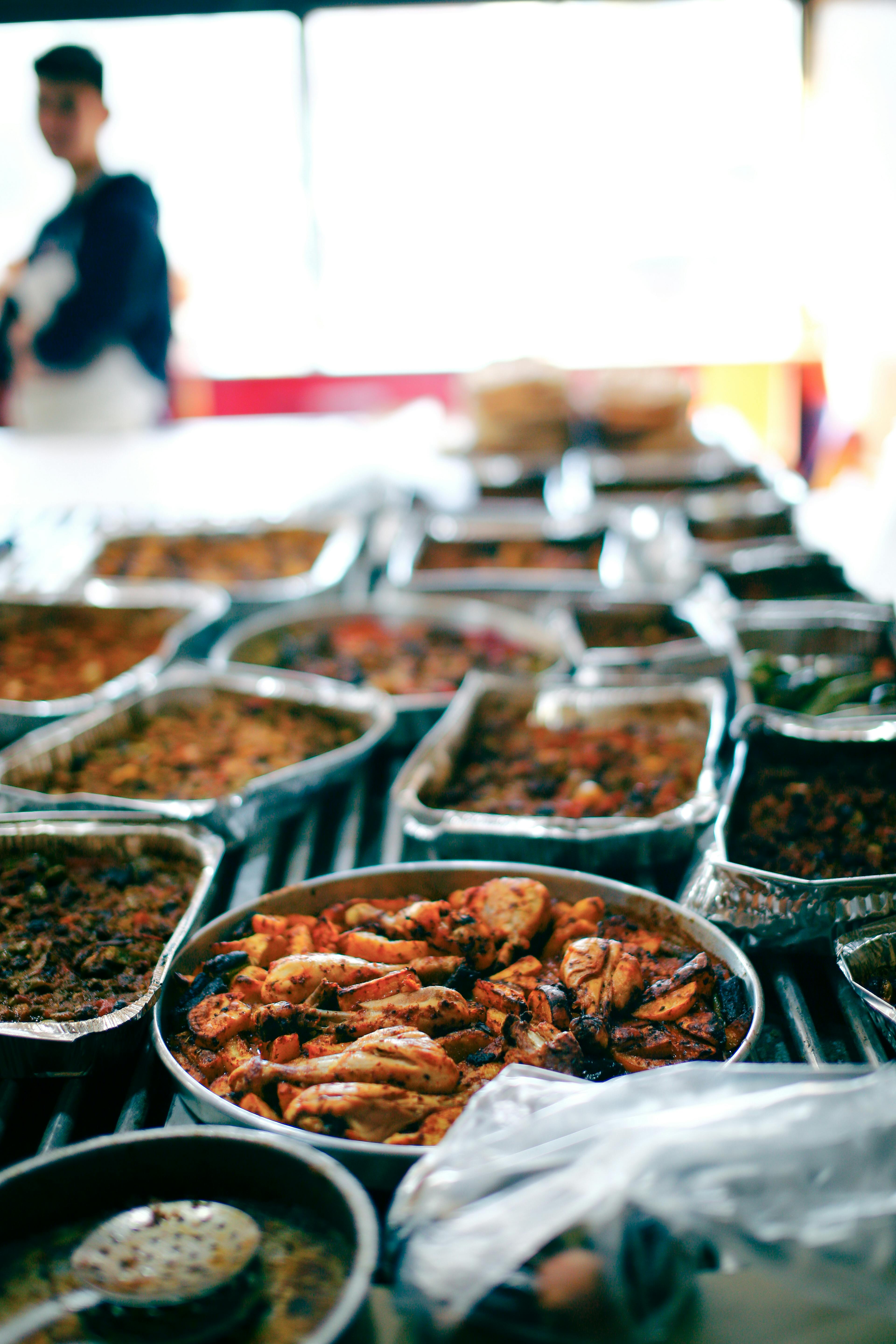 A variety of grilled meats served in aluminum trays at a bustling street food market. Perfect for food photography.